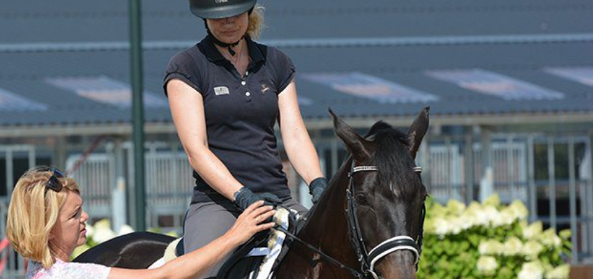 Trainer Dr. Britta Schoffmann is showing a rider how to hold their hands while riding.